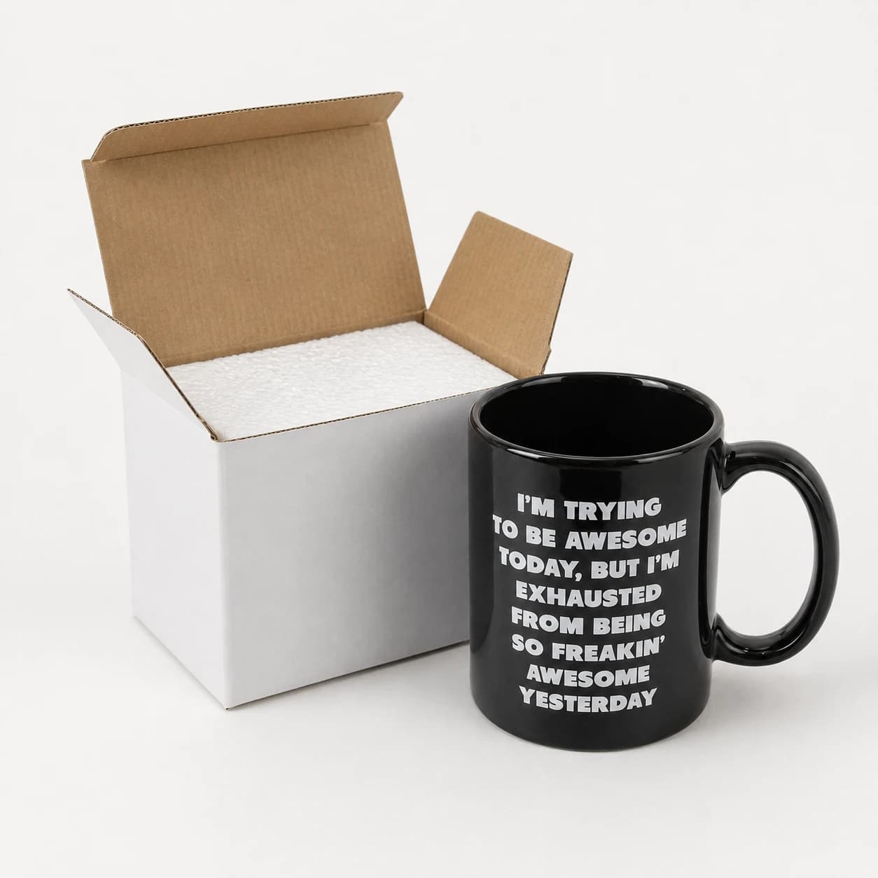 Glossy black slogan mug alongside its white carton and foam insert